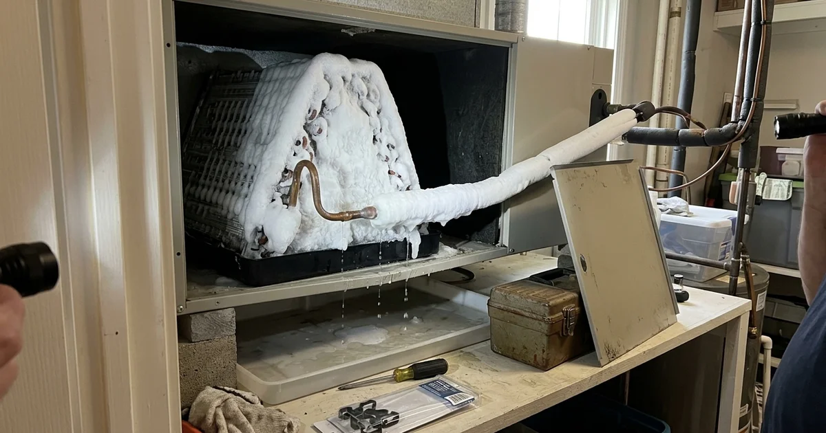 Ice built up on an indoor evaporator coil and refrigerant line inside an air handler